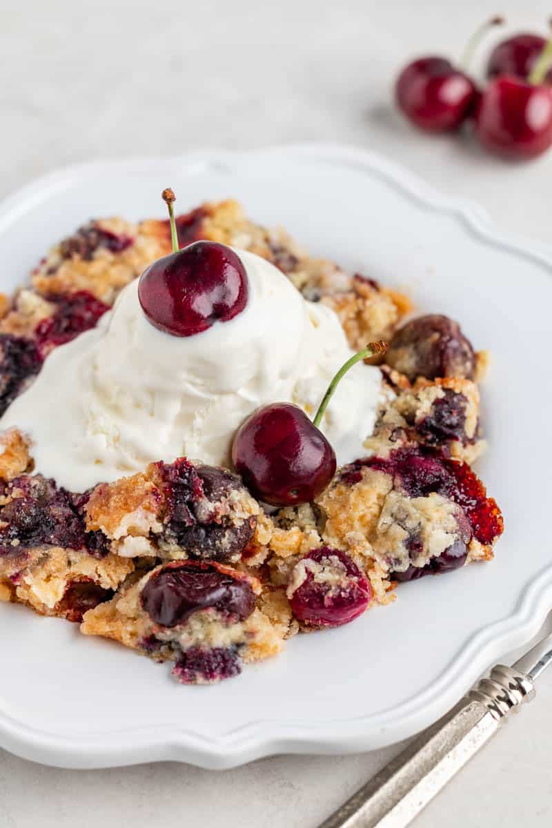 Cherry dump cake on a white dessert plate with ice cream on top.