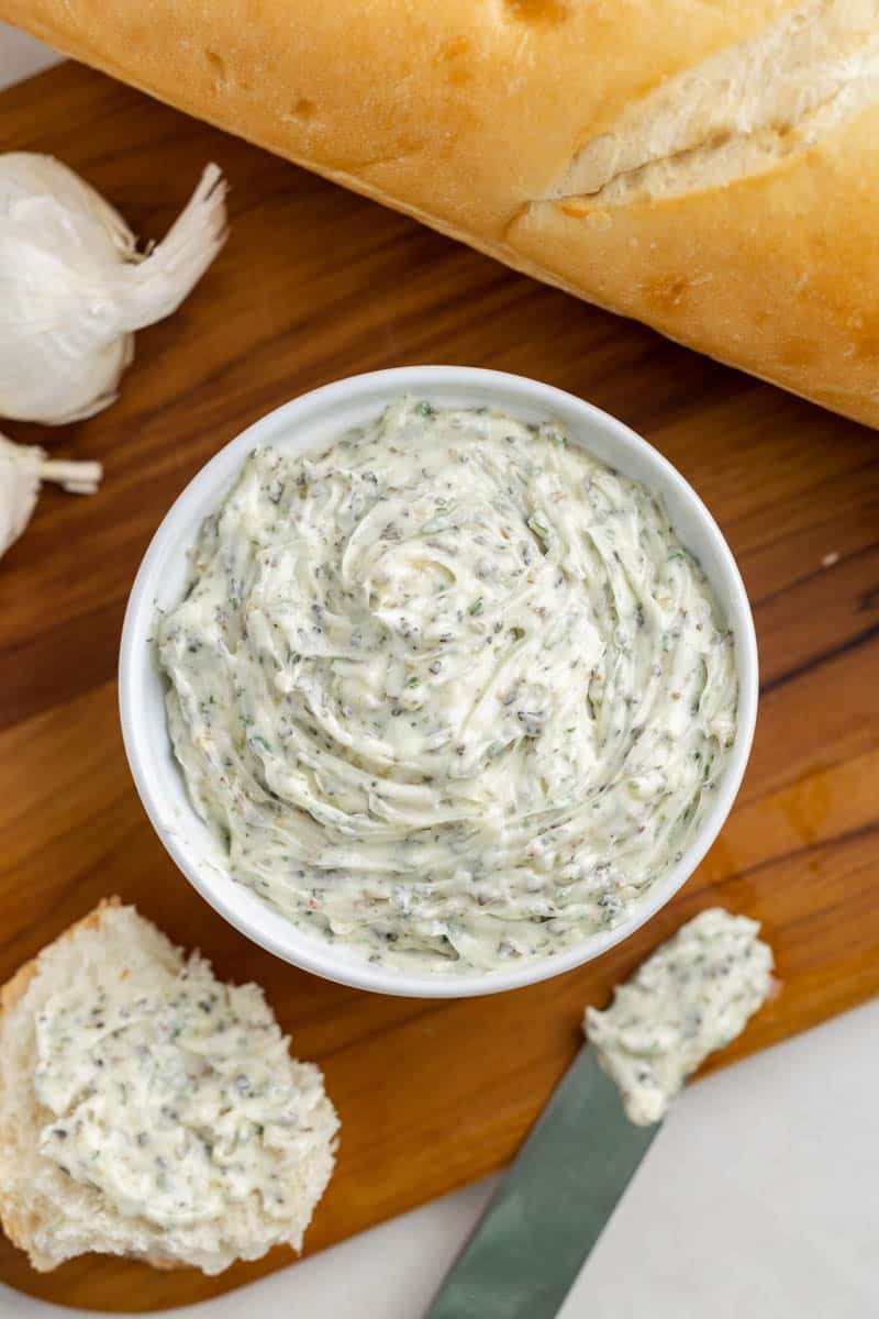 homemade garlic butter in a small white dish next to a loaf of French bread.