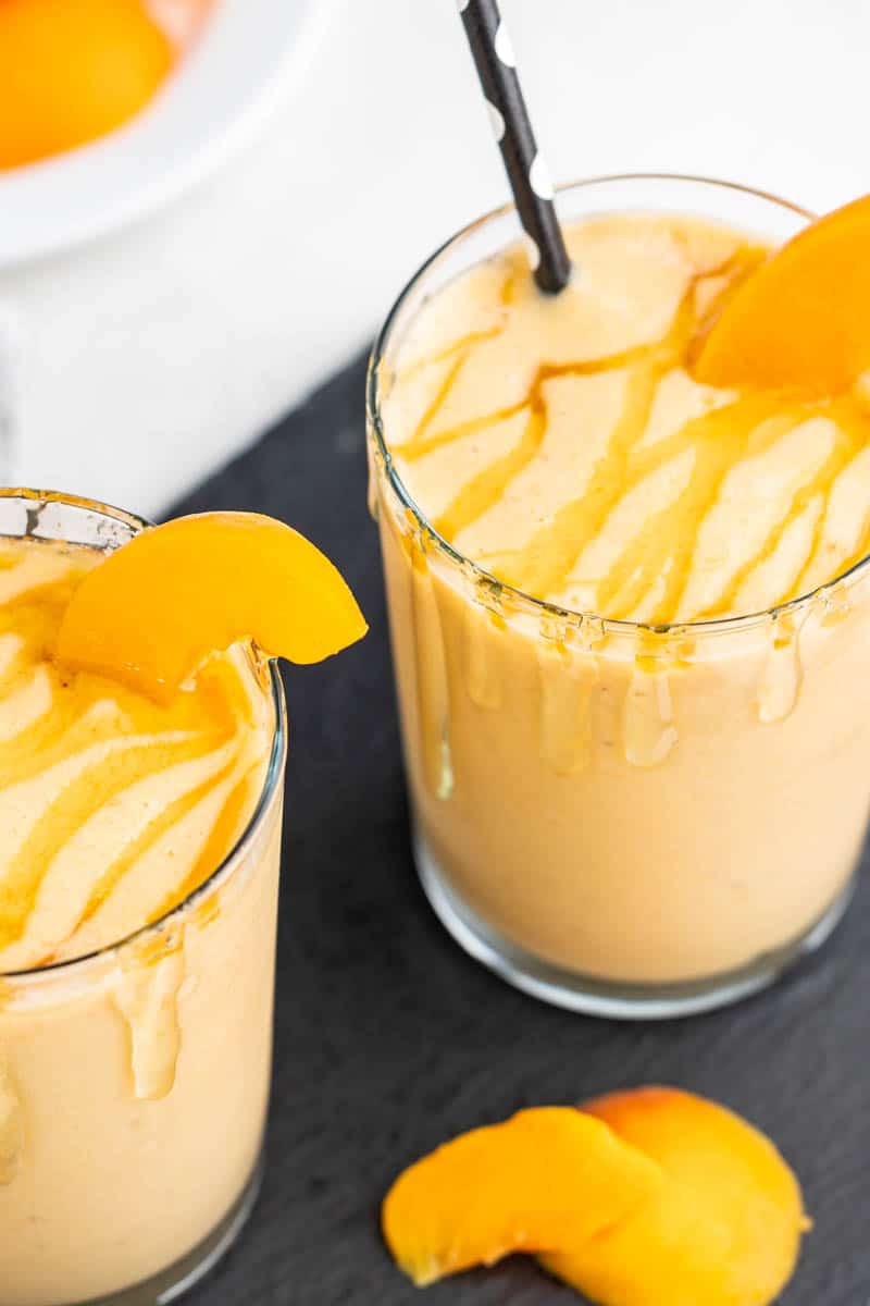 An overhead view of two peach smoothies in glasses with straws