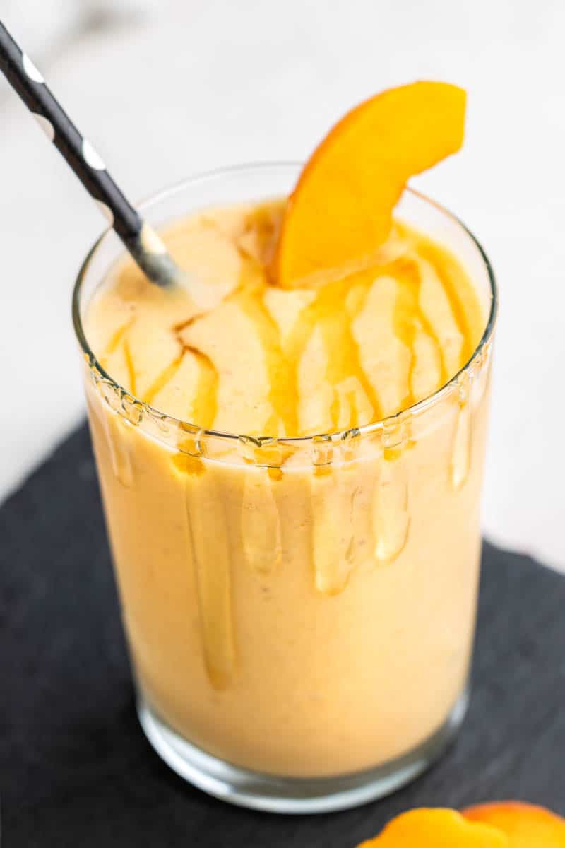 Close up view of a glass filled with a homemade peach smoothie on a black tray.
