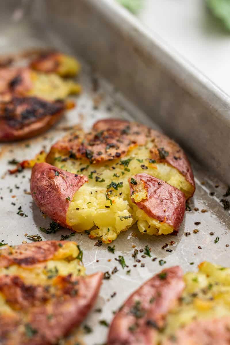 Close up view of garlic herb smashed potatoes on a baking sheet.