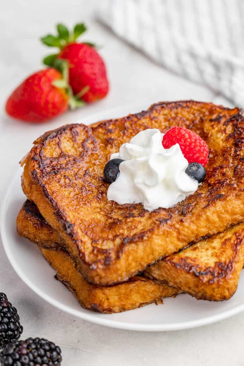 Overhead view of Crème brûlée French toast on a white plate surrounded by berries.