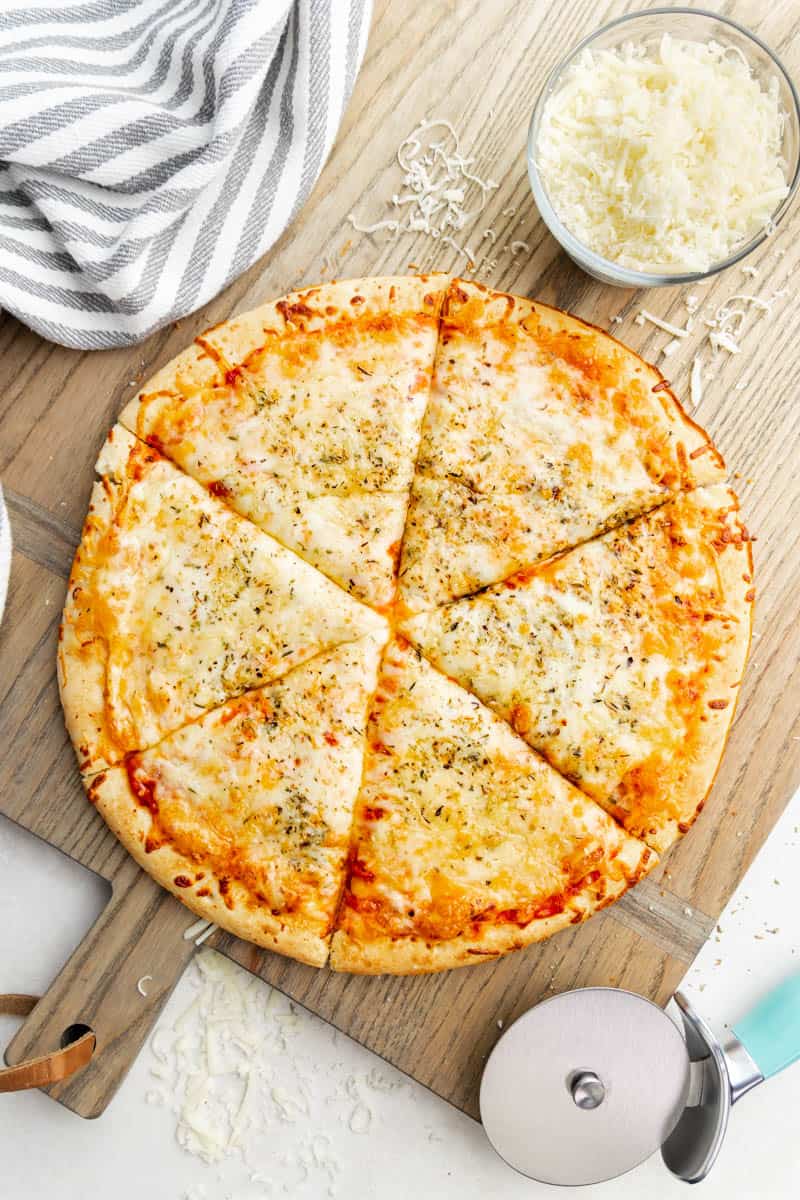 Overhead view of a cheese pizza on a wood cutting board.