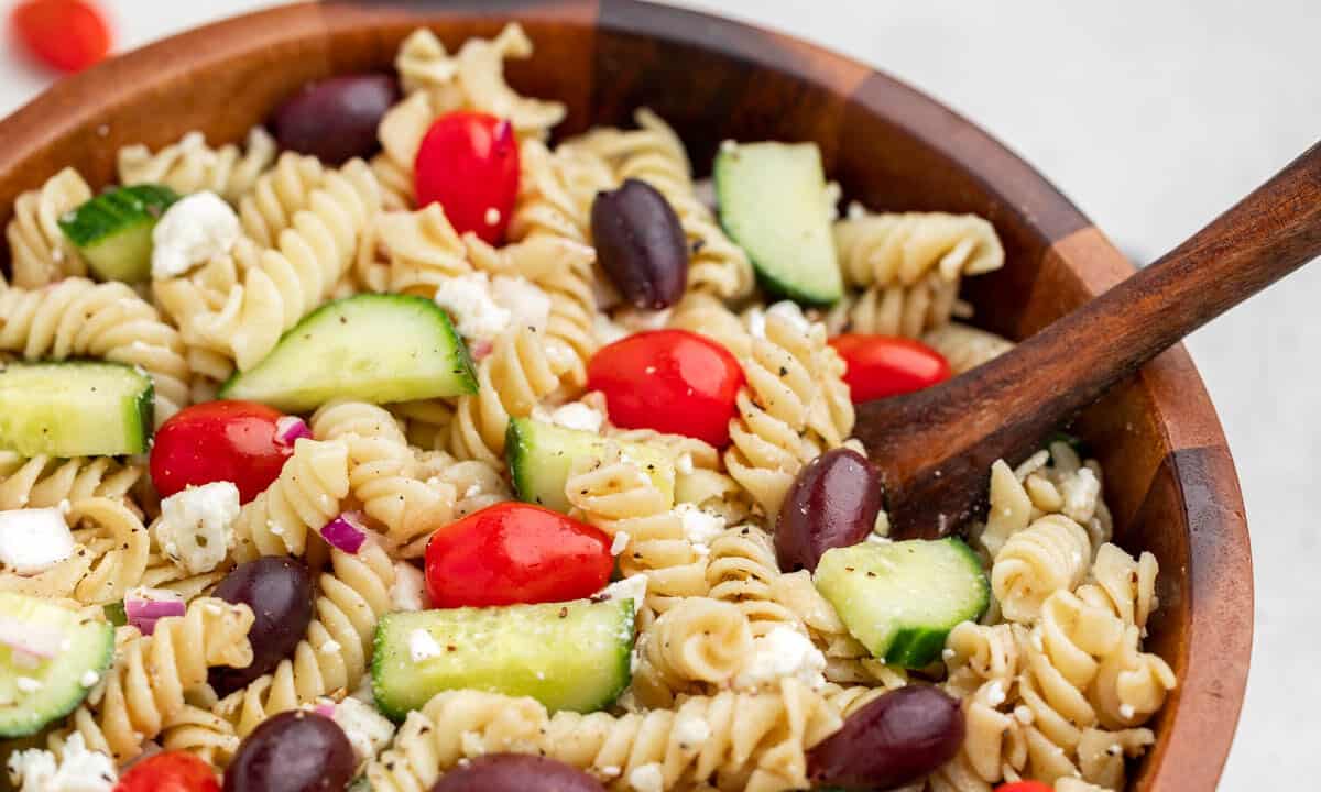 Close up view of greek pasta salad in a wood bowl.
