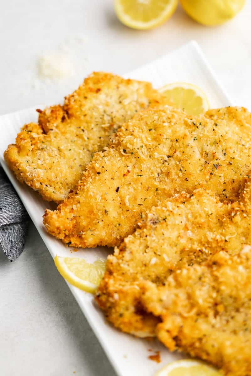 Close up view of parmesan crusted chicken on a white serving platter.