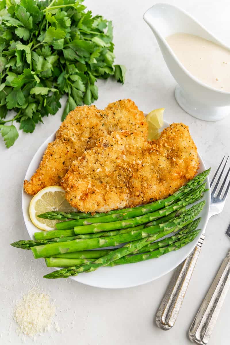 Overhead view of parmesan crusted chicken and veggies on a white dinner plate.