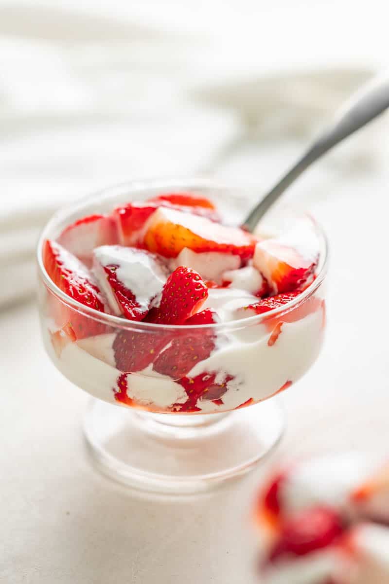 Strawberries and cream in a small glass jar with a spoon.