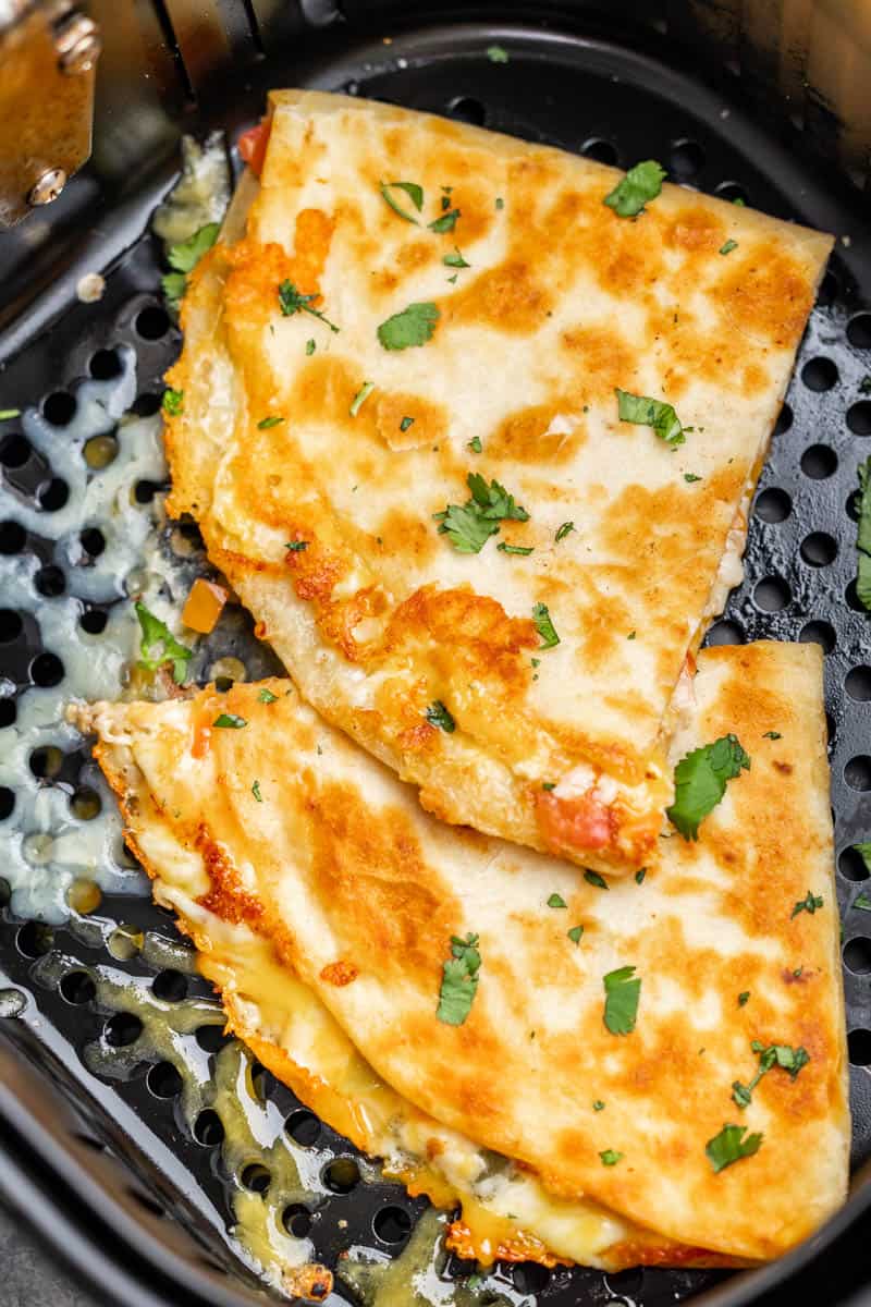 An overhead view of two cheese quesadillas in an air fryer basket.