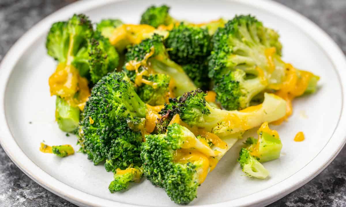 Cheesy air fried broccoli on a white dinner plate.