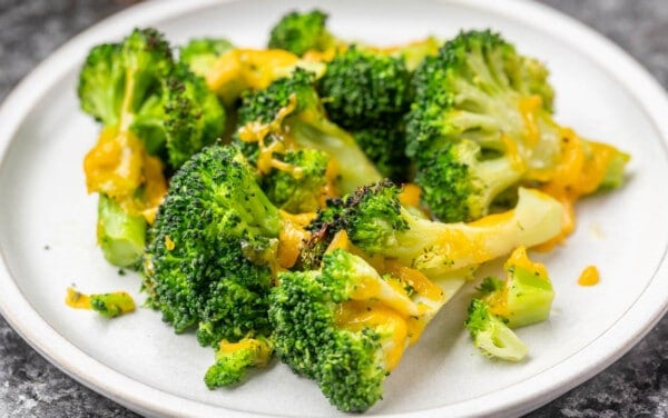 Cheesy air fried broccoli on a white dinner plate.