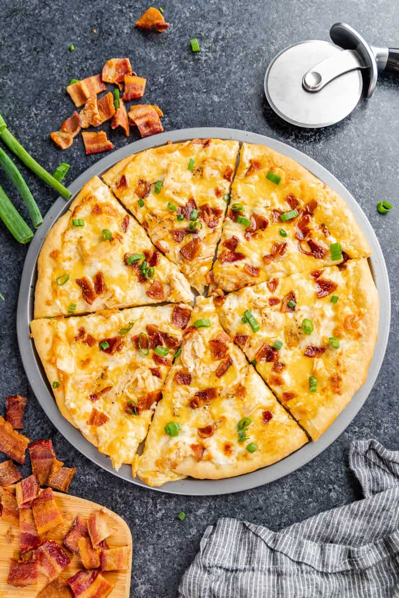 An overhead view of chicken bacon ranch pizza on a pizza pan.