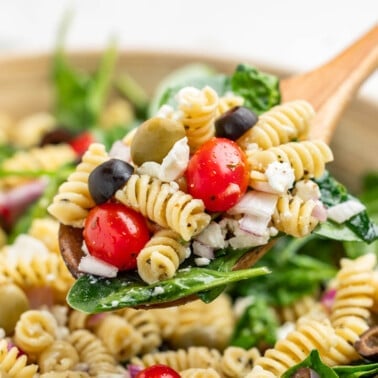 A wooden spoon filled with mediterranean pasta salad.