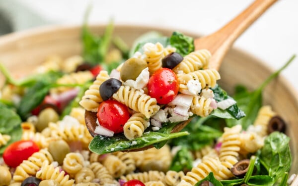 A wooden spoon filled with mediterranean pasta salad.