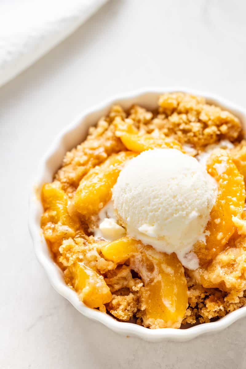 Overhead view of peach cobbler with a scoop of vanilla ice cream on top.