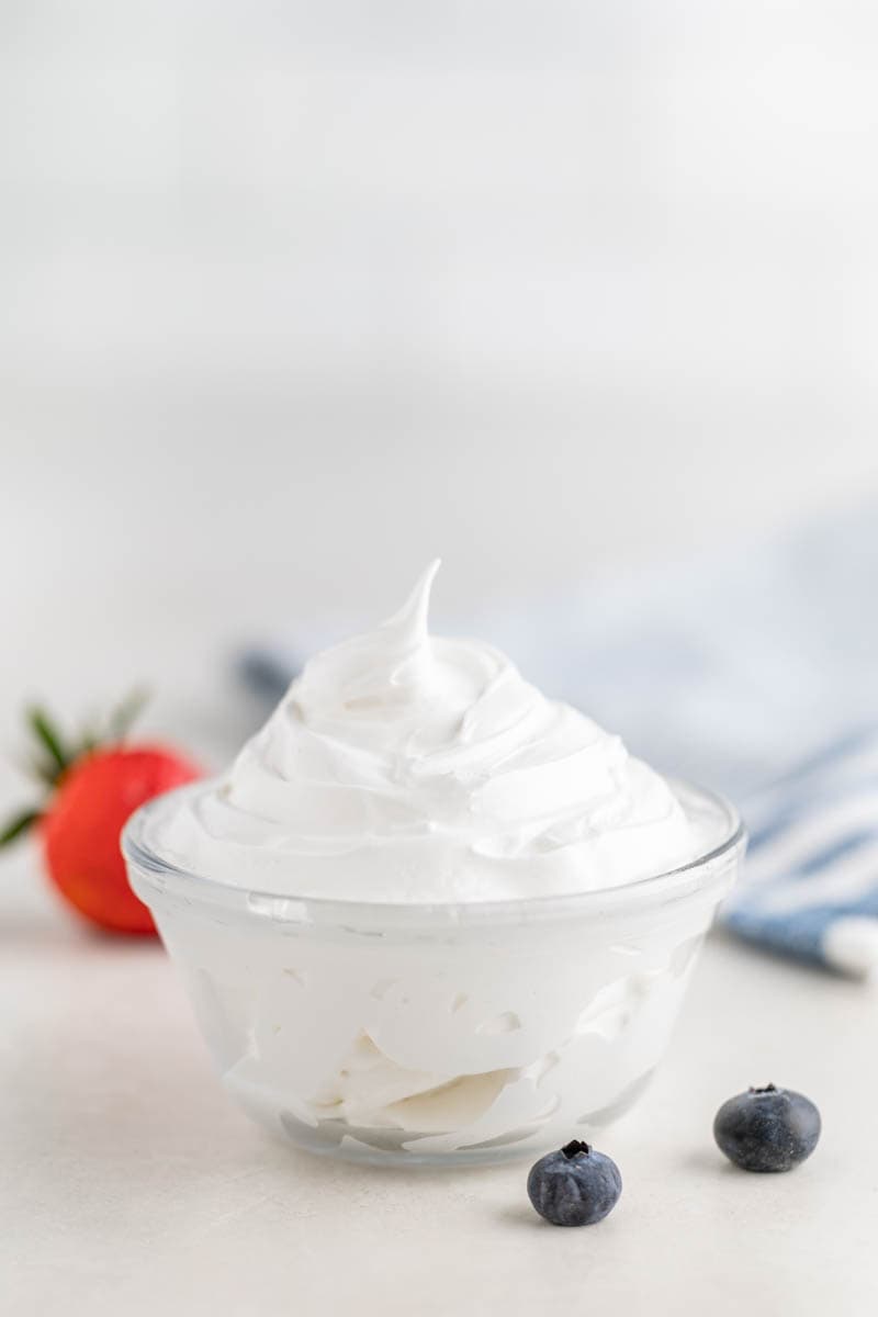 Homemade marshmallow fluff in a small glass bowl, surrounded by fresh berries.