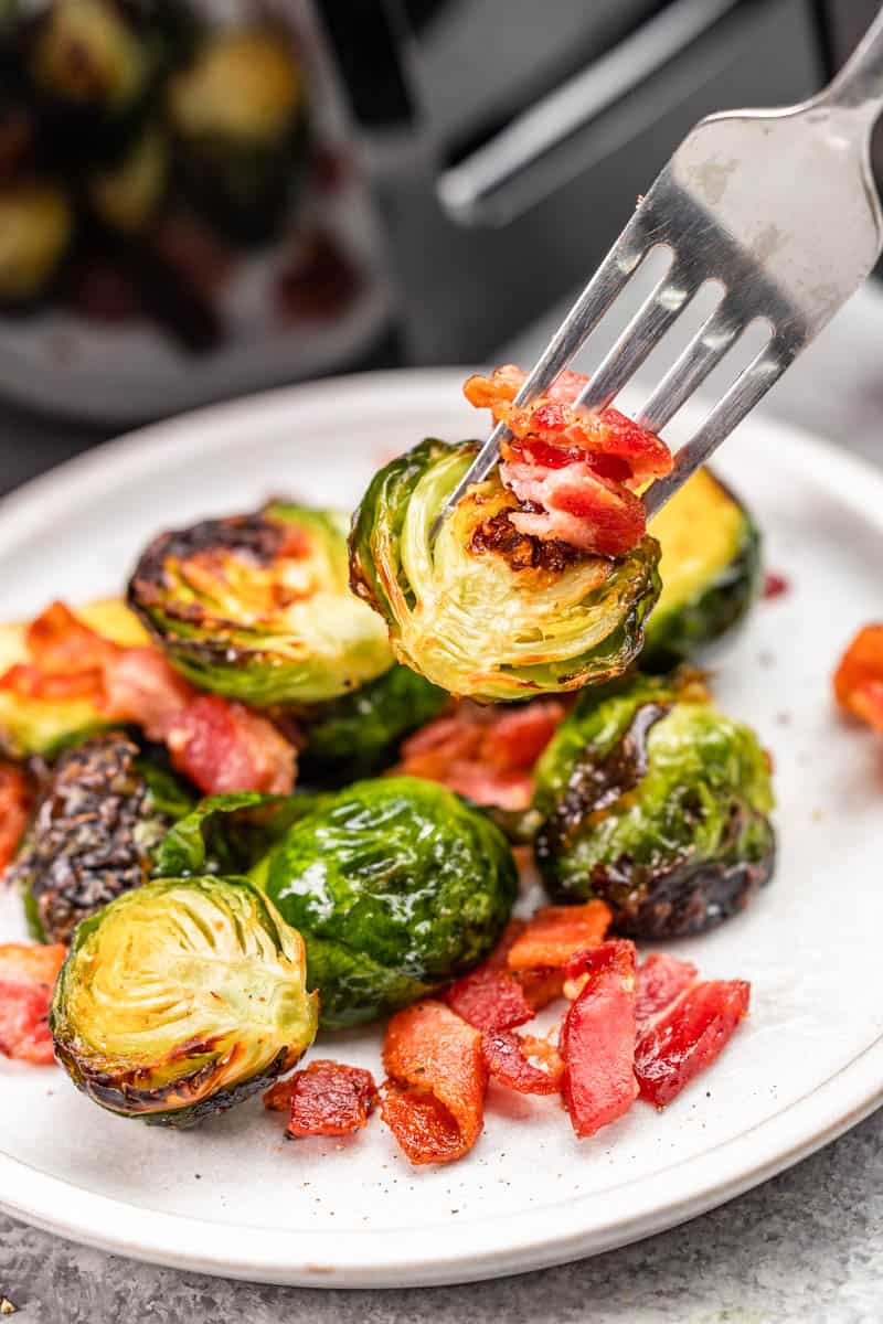 A fork with brussels sprouts and bacon on top, hovering over a plate.
