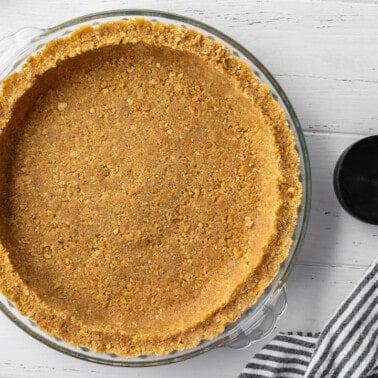 Graham cracker crust in a glass pie plate on a wood table.