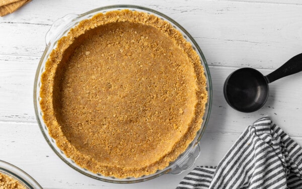 Graham cracker crust in a glass pie plate on a wood table.