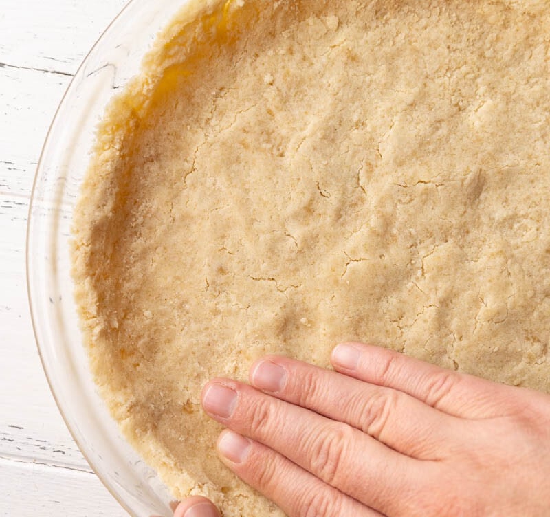 A hand pressing a shortbread graham cracker pie crust into the pie plate.