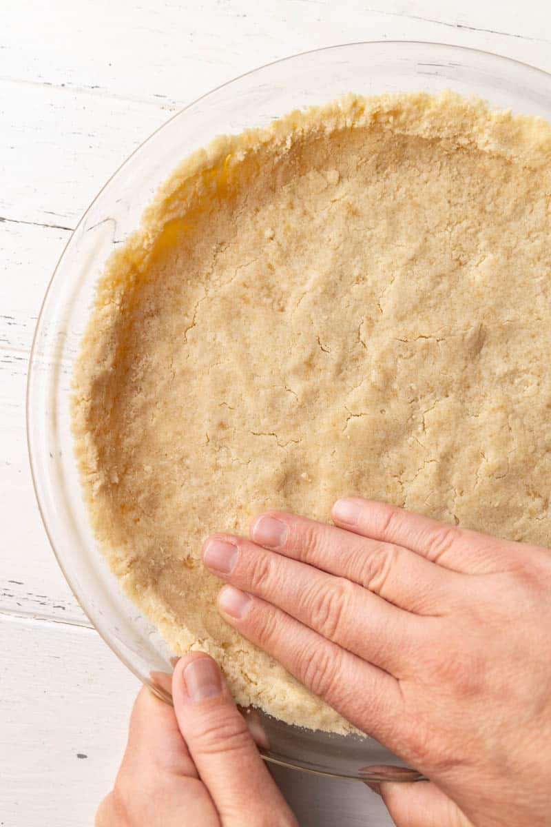 A hand pressing a shortbread graham cracker pie crust into the pie plate.