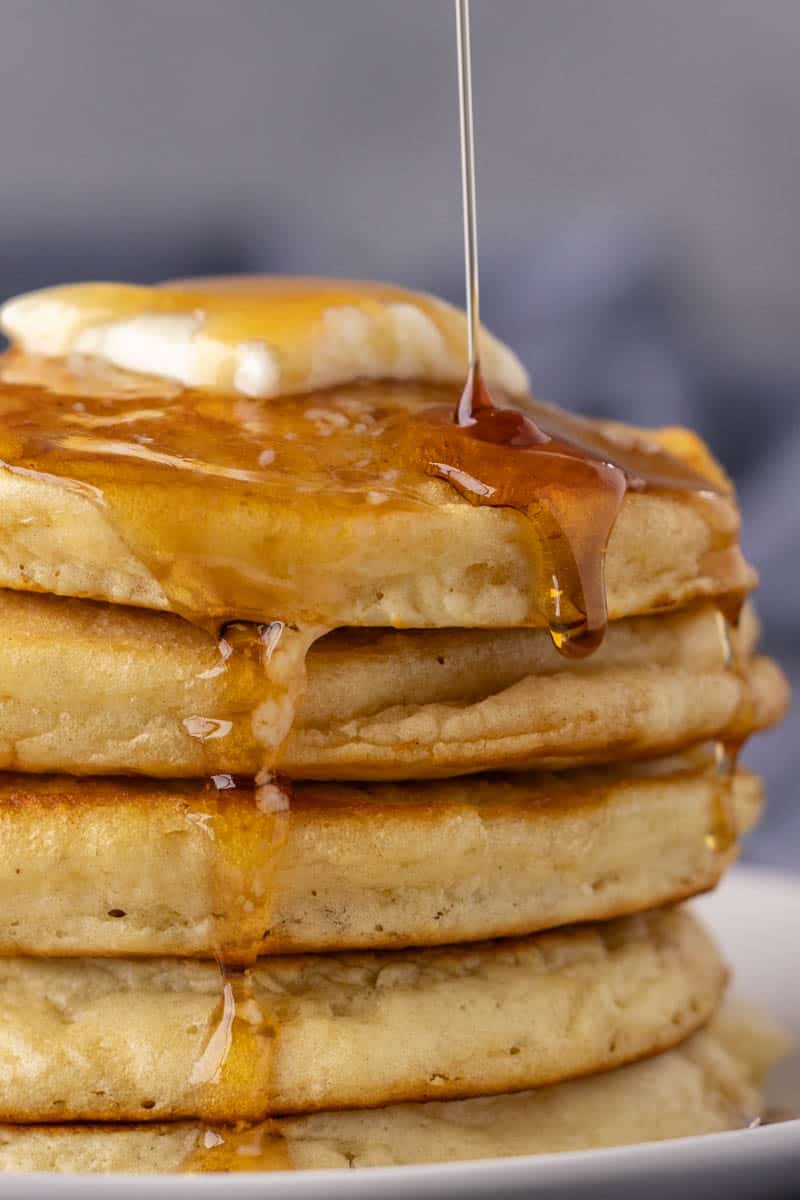 A large stack of pancakes with syrup being drizzled on top.