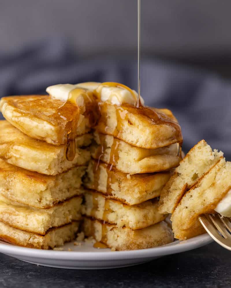 A stack of thick pancakes with a pat of butter on top and syrup being drizzled over the top.