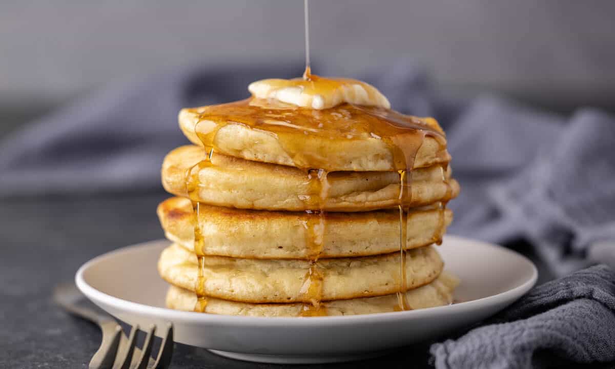 A stack of pancakes with syrup being drizzled over the top.