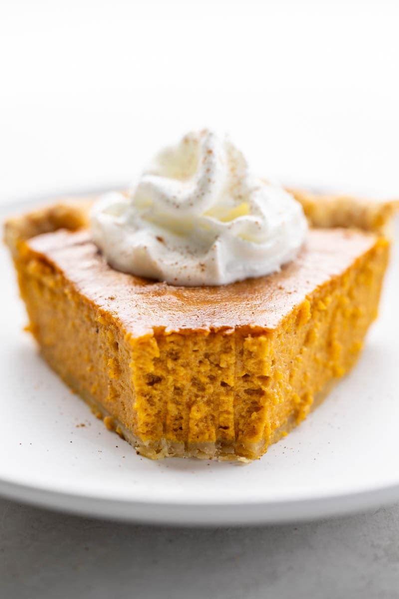 Eye level, head-on view of a piece of pumpkin pie with a bite removed.