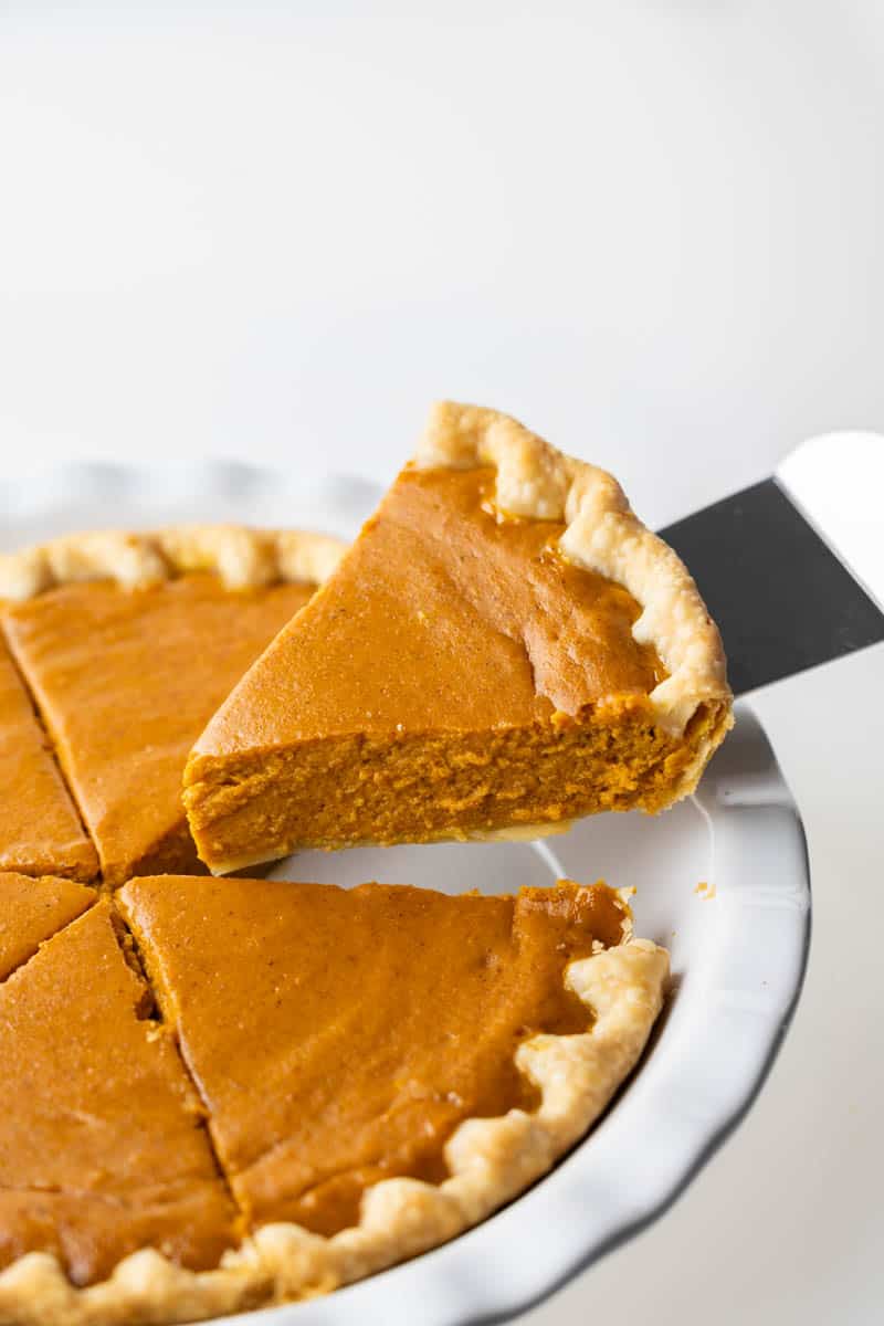 A spatula pulling a piece of pumpkin pie out of the pie plate.