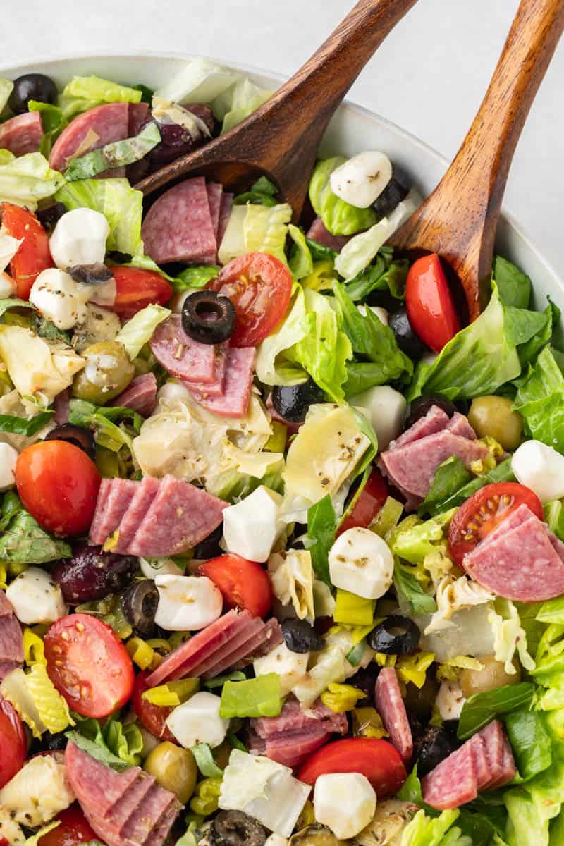 Overhead view of an antipasto salad in a serving bowl with wooden spoons.