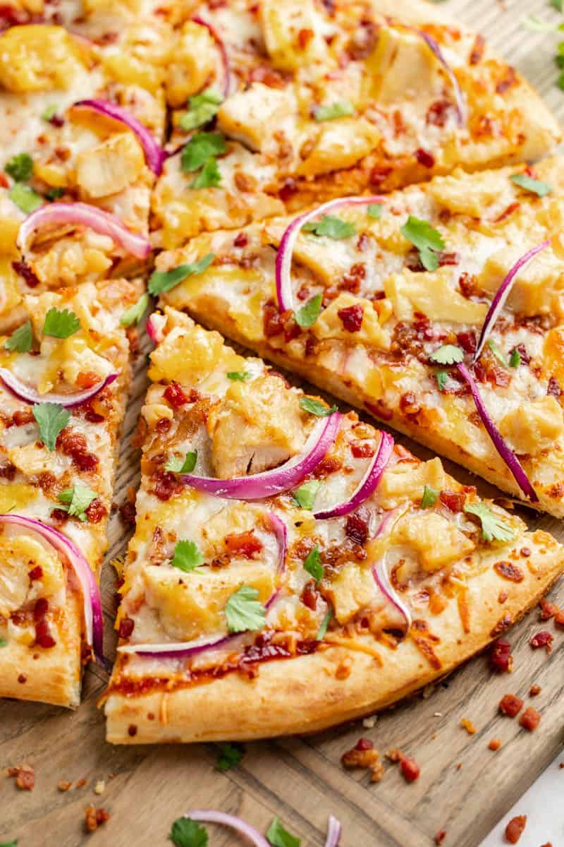 Overhead view of a bbq chicken pizza cut into slices on a wood serving platter.