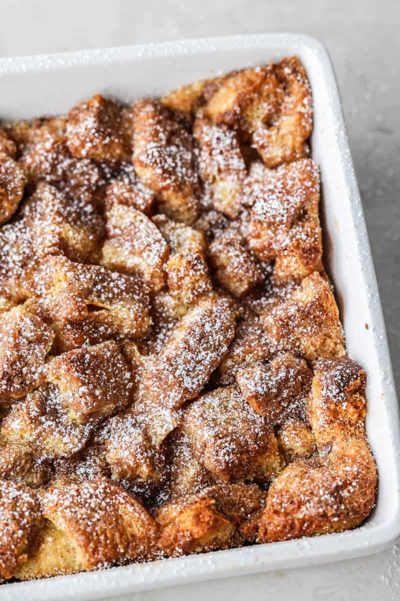 French toast casserole with powdered sugar dusted on top in a white baking dish.