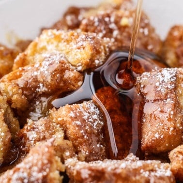 Close up view of maple syrup being poured onto a serving of French toast casserole on a white plate.