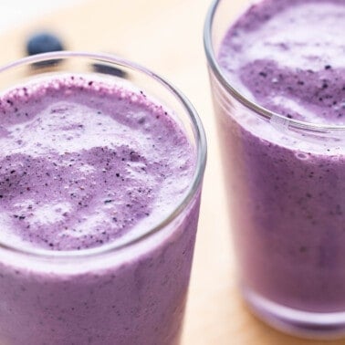 Close up view of blueberry smoothies in tall, clear glasses.