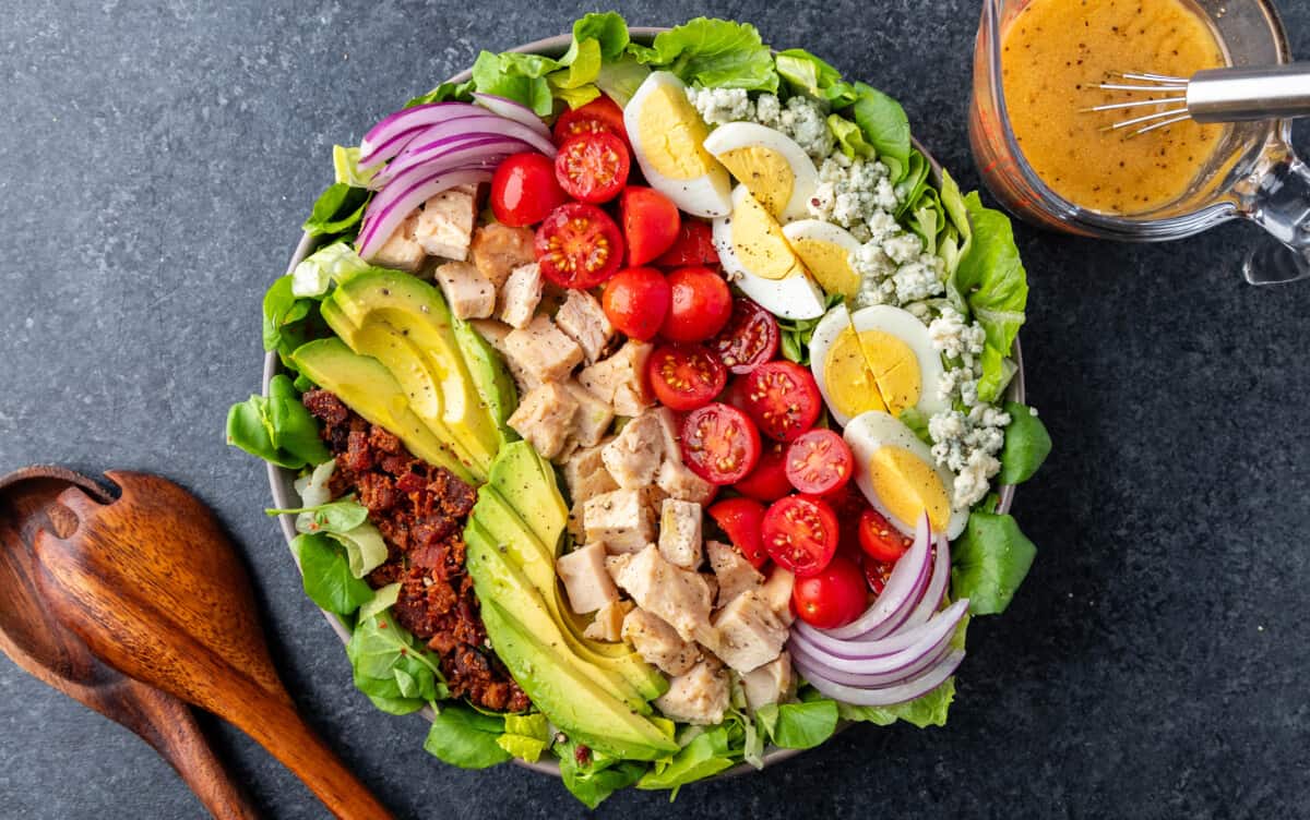 Overhead view of a large Cobb Salad with wooden spoons on the side.