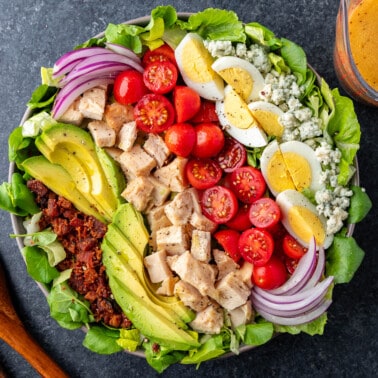 Overhead view of a large Cobb Salad with wooden spoons on the side.