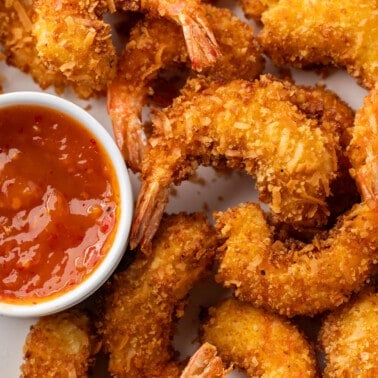 Overhead view of crispy coconut shrimp with dipping sauce on a serving platter.