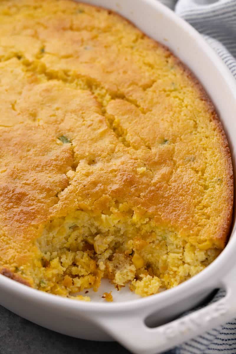 Close up view of a corn casserole in a baking dish with a serving removed.