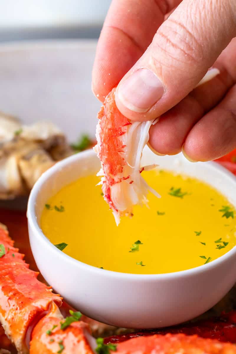 A hand dipping a small piece of crab meat into melted butter.