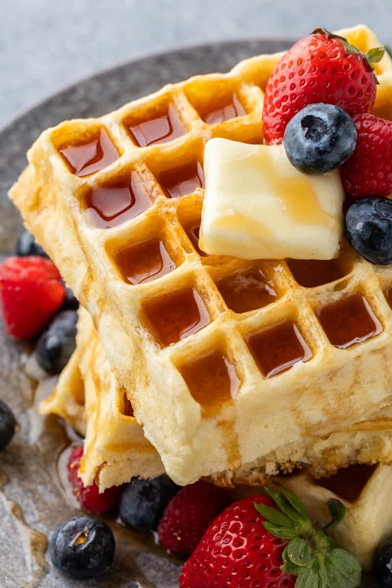 Close up, overhead view of a stack of homemade waffles with a pat of butter and fresh berries on top.