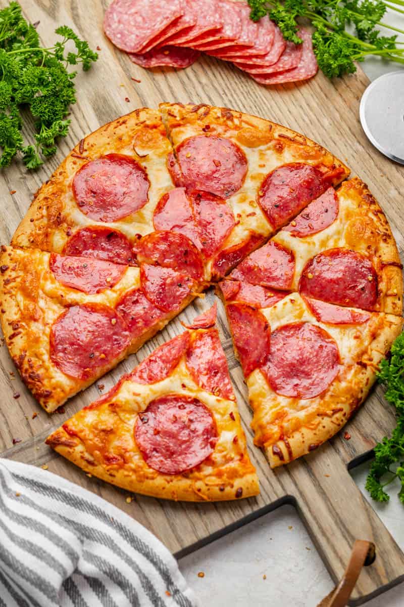 An overhead view of salami pizza on a wood tray.