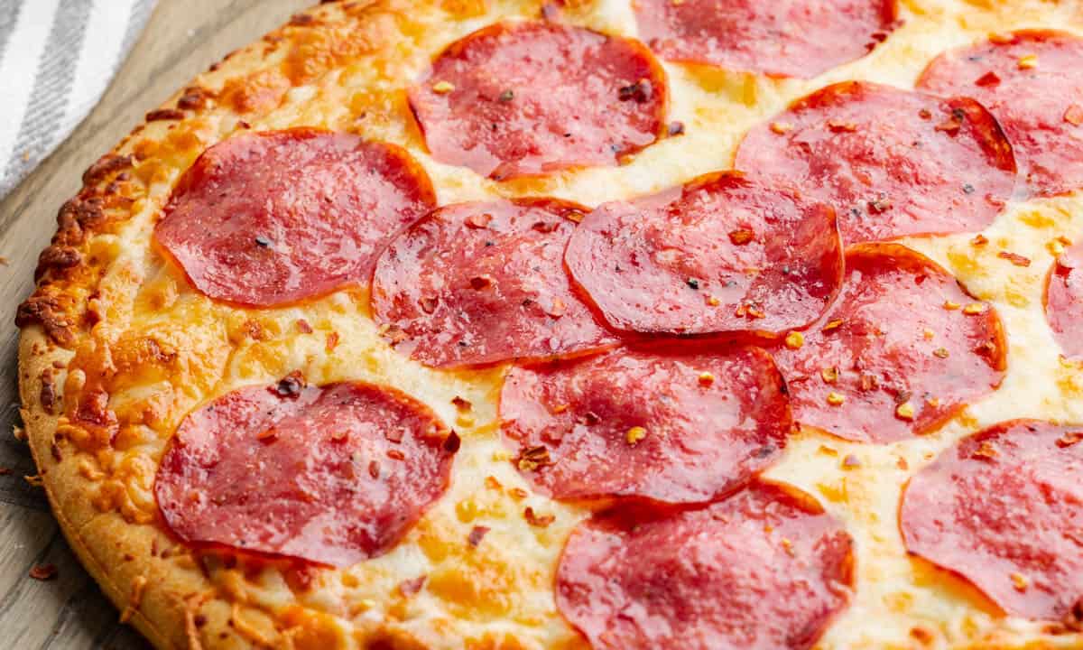 Close up view of a salami pizza on a wood tray.