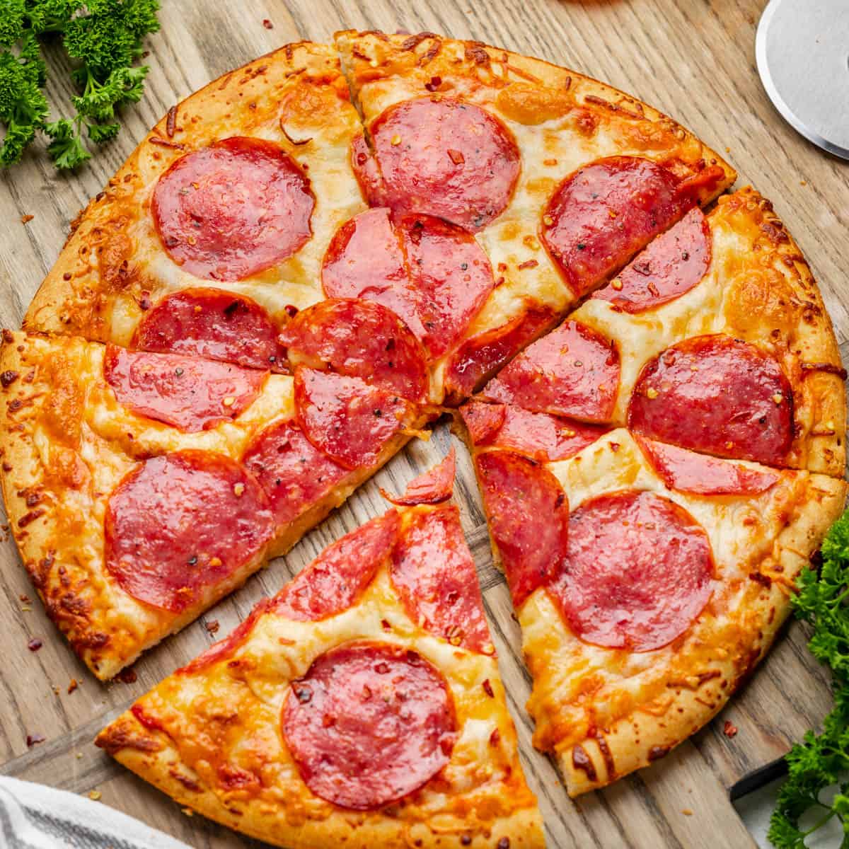 An overhead view of a salami pizza sliced into pieces on a wood board.