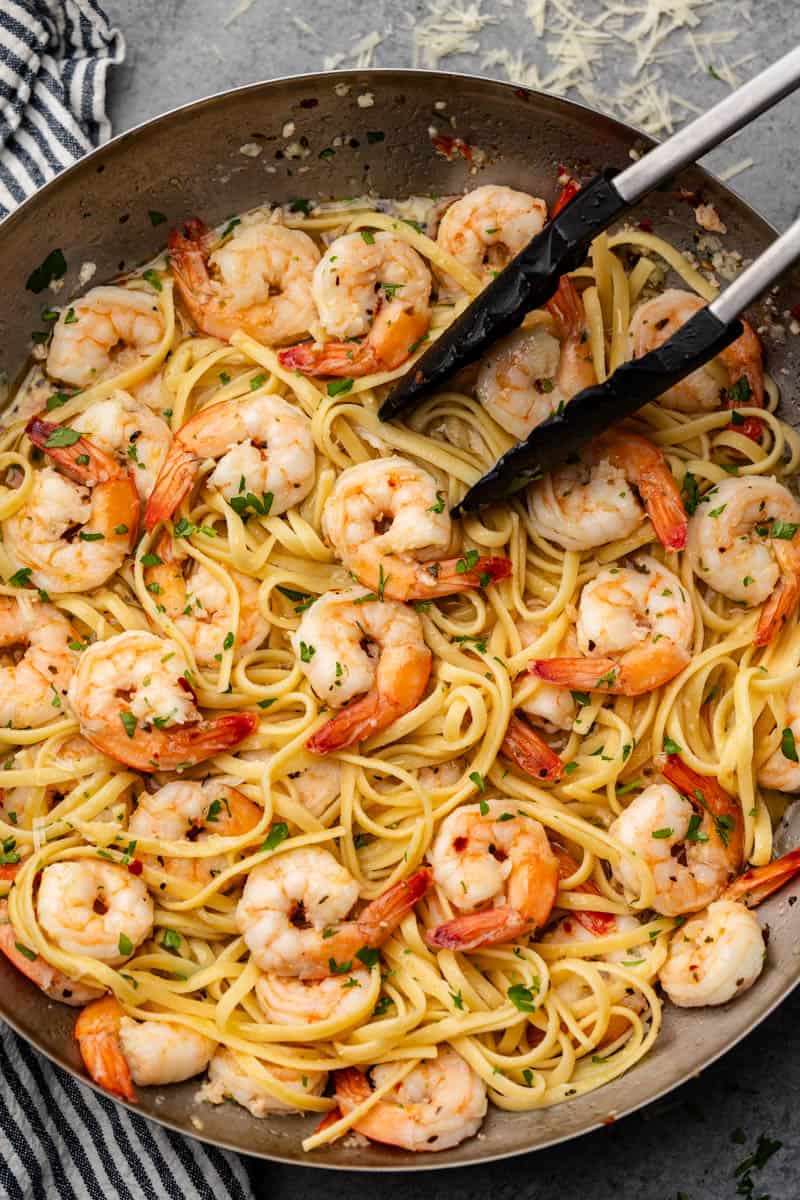Overhead view of shrimp scampi with tongs in a skillet.