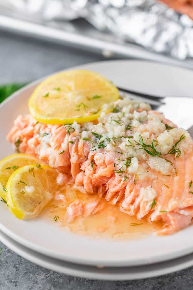 A serving of baked salmon with lemon slices on top on a small dinner plate.