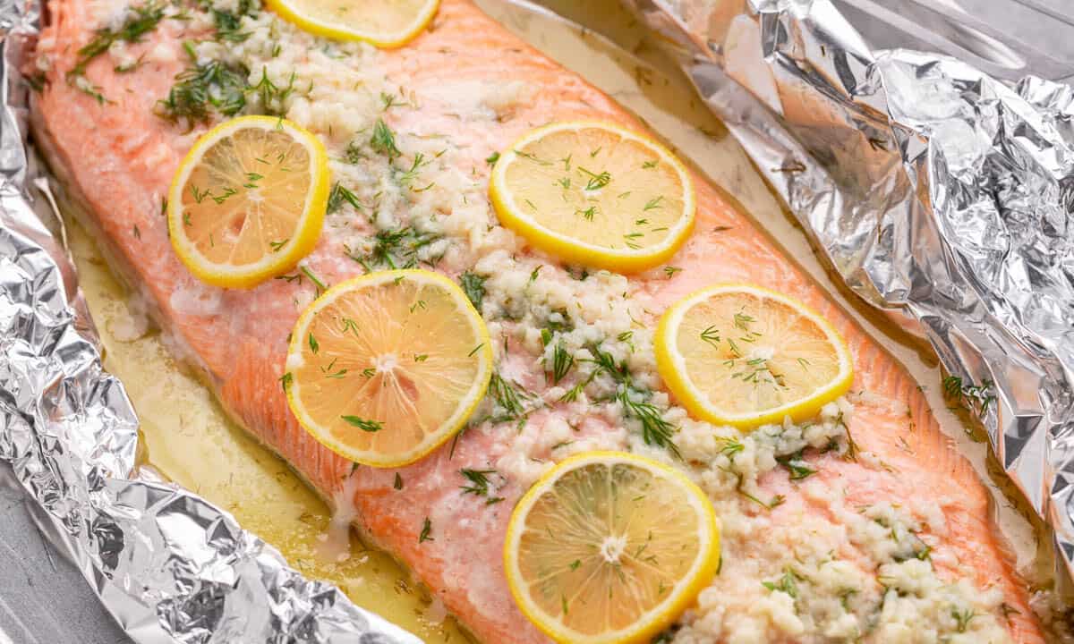 Close up view of a whole baked salmon filet with garlic and lemon slices on top.