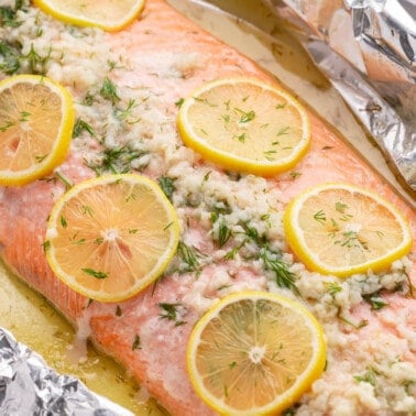 Close up view of a whole baked salmon filet with garlic and lemon slices on top.
