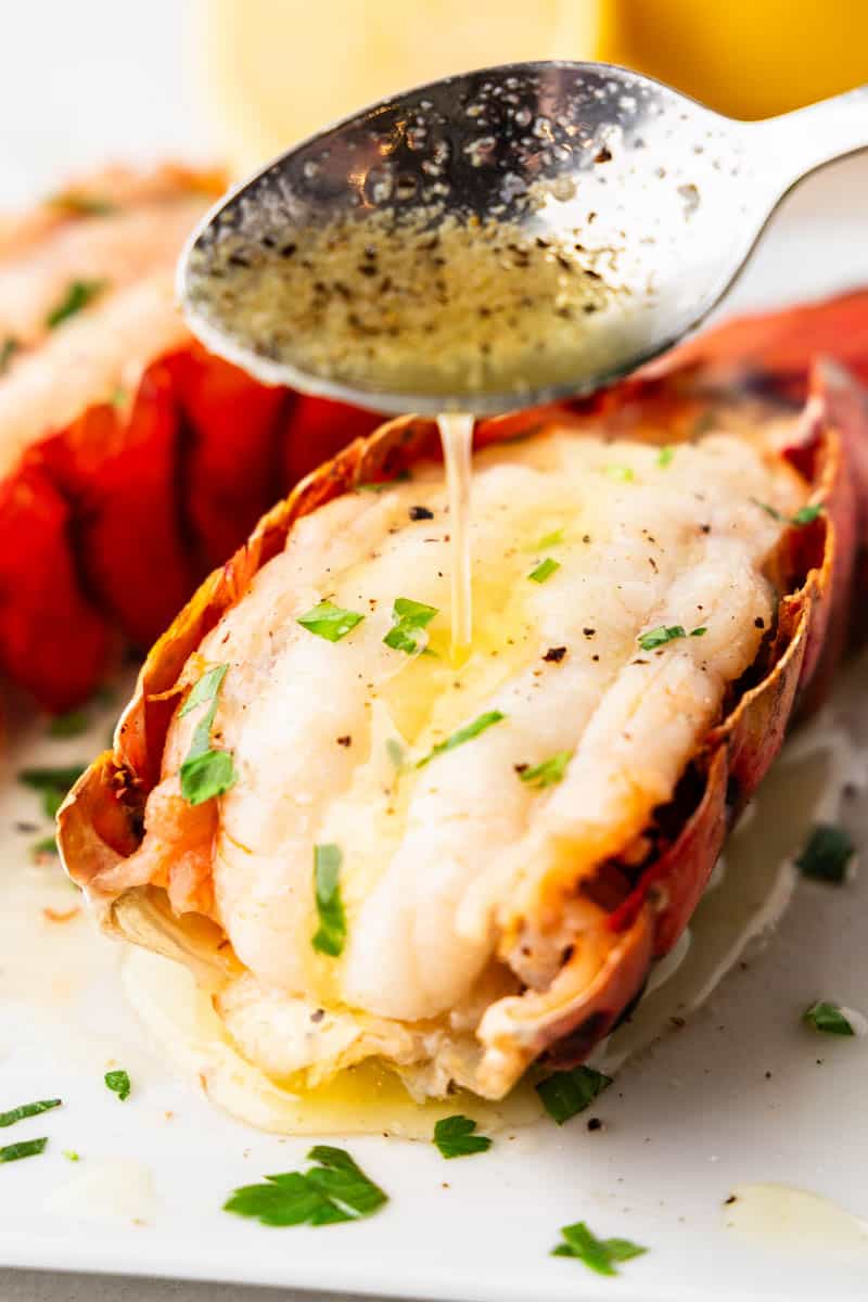 A spoon drizzling melted buttre onto broiled lobster tails.