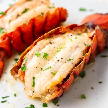 Close up view of broil lobster tails on a white serving platter.