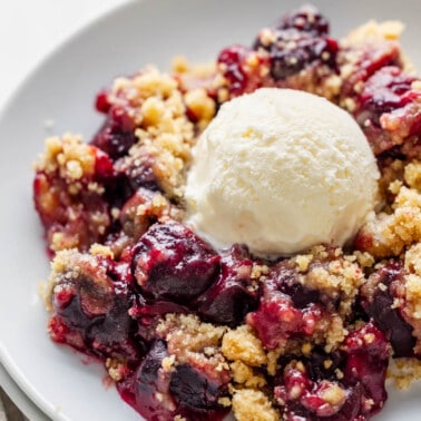 A serving of cherry crumble with vanilla ice cream on top.